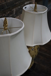 Two white lampshades with gold fixtures on a dark surface.