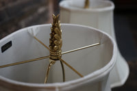 Close-up of a gold lampshade finial on a white lampshade with a blurred background.