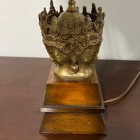 Stunning and unique vintage table lamp. It sits on a wood base. There are 4 crowned asian female faces as part of the base. They appear to be cast in brass or bronze. 