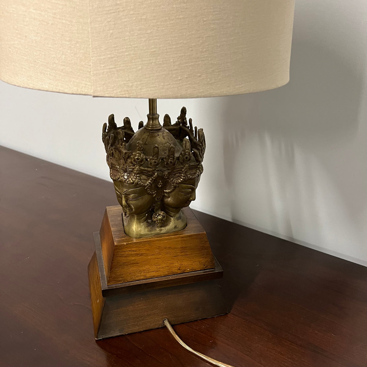 Stunning and unique vintage table lamp. It sits on a wood base. There are 4 crowned asian female faces as part of the base. They appear to be cast in brass or bronze. 