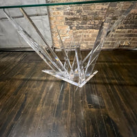 A console table with a glass top and lucite base that almost appears to be stalagmites or ice crystals