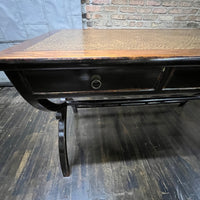 Black lacquer desk that has two "S" shaped legs that cross each other (a sort of hourglass shape). &nbsp;There is a smooth rattan inlay set within the desk's work surface. &nbsp;It has three drawers for storage with simple hardware.