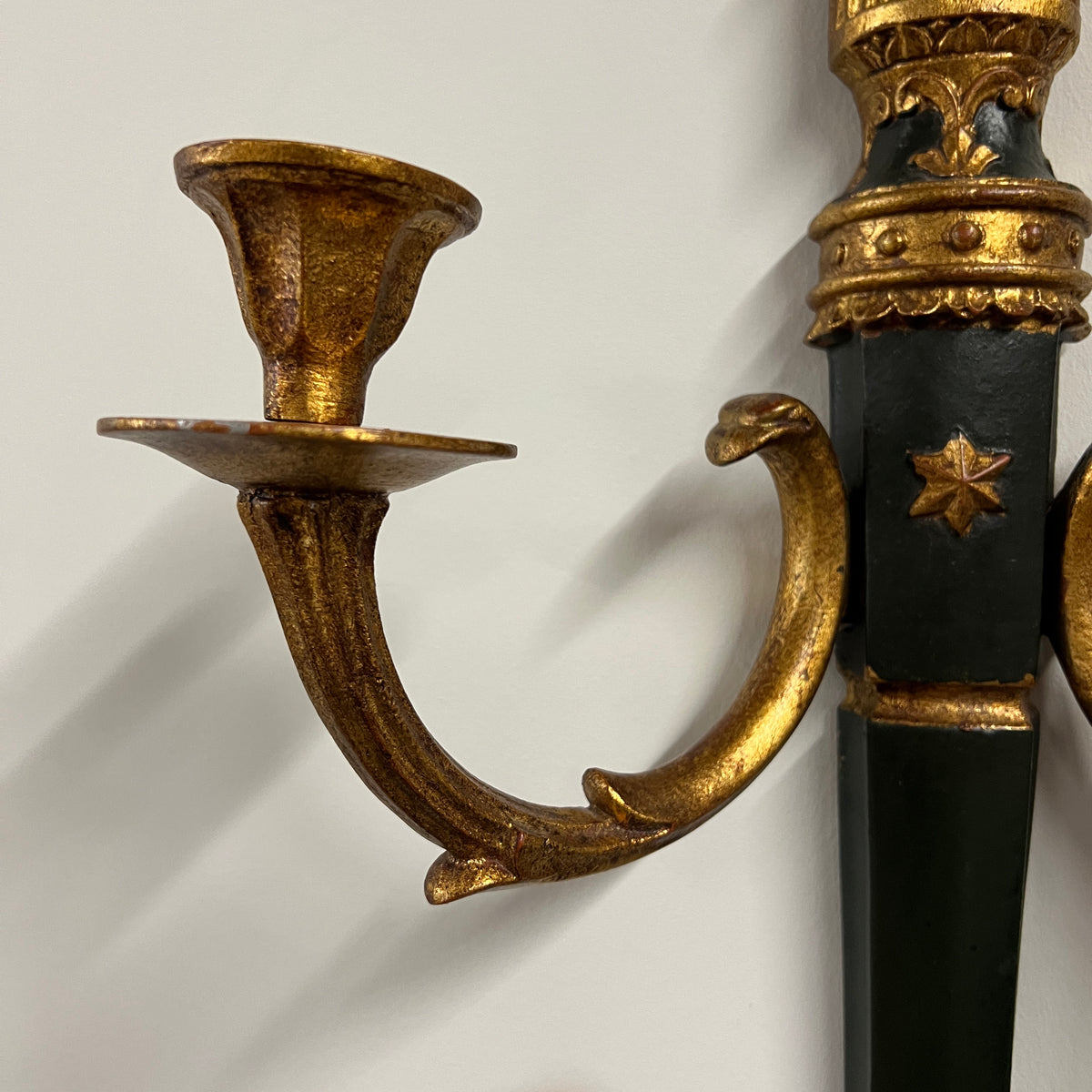 A pair of elegant wall sconces that feature an ebonized center and parcel-gilt stem supporting two gilt metal candle arms adorned with detail in the style of Louis XVI. Each center body is accented with a raised gold colored star. On the back are Palladio labels and markings.