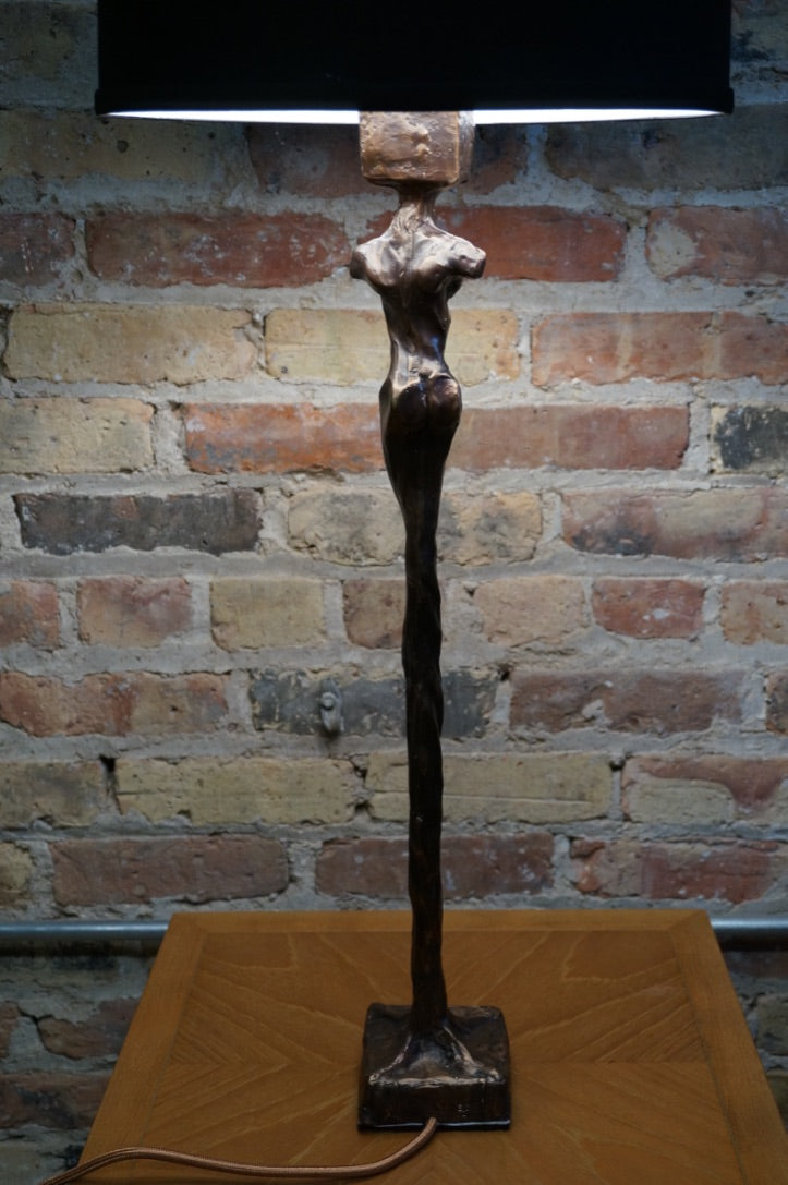 Limited Edition.  Signed and numbered bronze sculptures grace the base of this stunning table lamp that is often mistaken for a Giacometti styled female figure.   Two versions (similar yet not identical) make the perfect pair of lamps.  Rooted melds art (sculpture) and function (lamp).  Exclusive to Studio Sonja Milan.