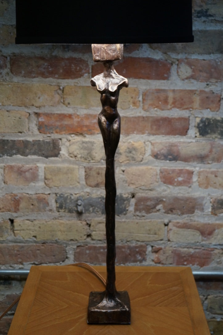 Limited Edition. Signed and numbered bronze sculptures grace the base of this stunning table lamp that is often mistaken for a Giacometti styled female figure. Two versions (similar yet not identical) make the perfect pair of lamps. Rooted melds art (sculpture) and function (lamp). Exclusive to Chicago location.